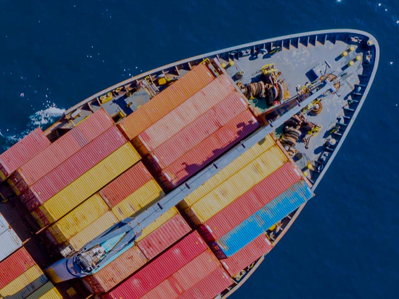 Aerial view of a large container ship loaded with colorful cargo containers, traveling on the blue ocean